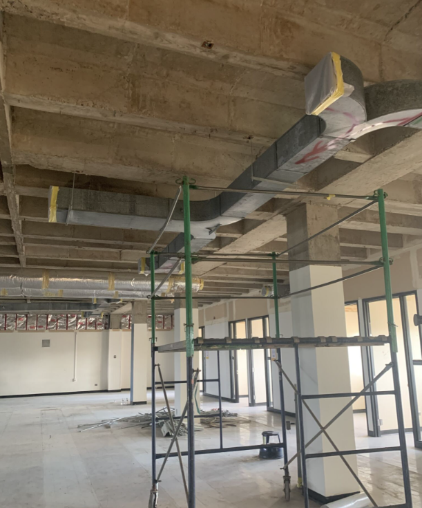 An empty room with ceiling and vent exposed. A green and silver scaffold is in the foreground.