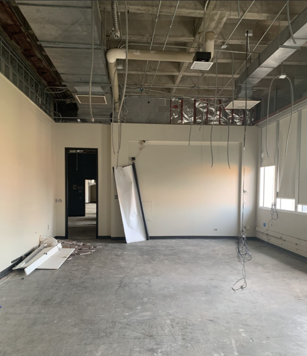 An empty room with ceiling and vent exposed. A projector screen is on the ground along with other debris.