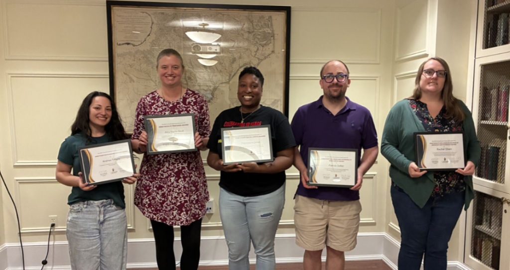 Five people standing shoulder to shoulder holding framed certificates and smiling.