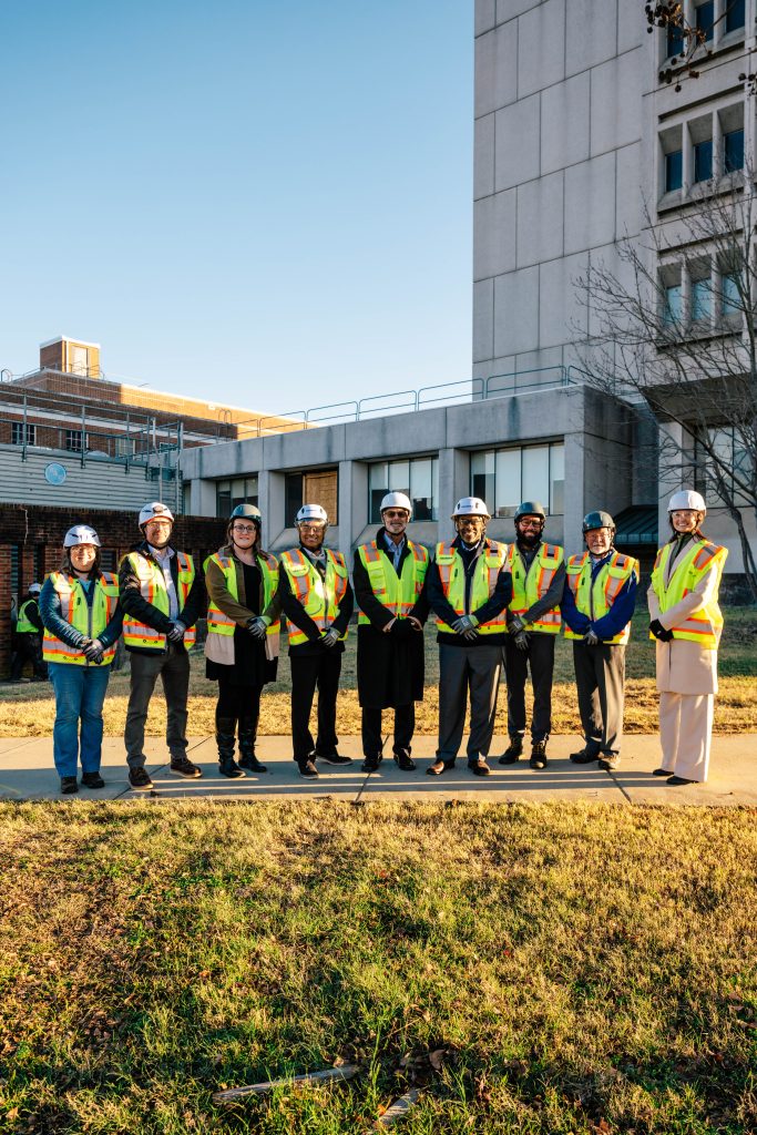 Nine people standing shoulder to shoulder wearing construction hats and safety vests.